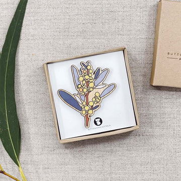 A wooden brooch painted and shaped like a golden wattle inside a box.