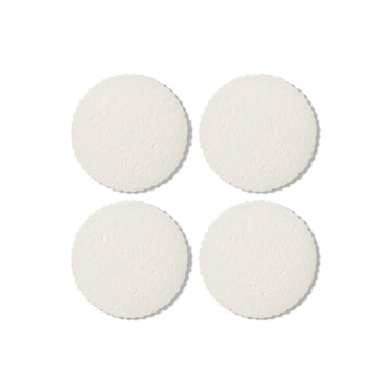 A set of four round white coasters with scalloped edges.