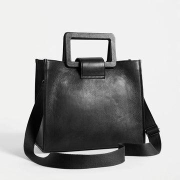Front view of a black leather tote bag with a rectangle handle and a long cross body strap.