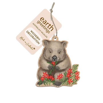 Wooden decoration of a wombat holding flowers with 'earth greetings' tag on a white background.