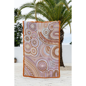 Decorative throw blanket with circular pattern on a white surface with palm tree in background.
