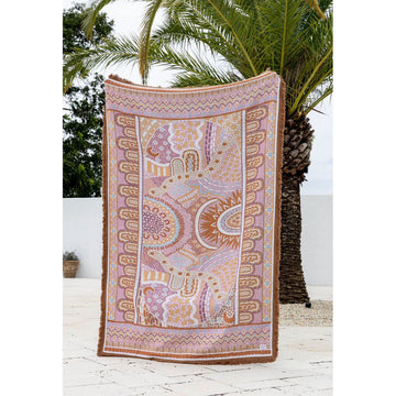 A pink patterned throw hanging up with palm trees in the background.