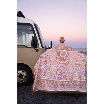A pink patterned throw hanging up with palm trees in the background.