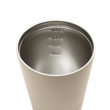 A reusable coffee cup in a light oat brown with a black lid and the text 'made by Fressko' on the bottom.