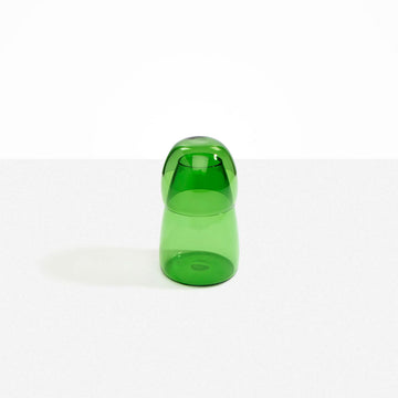 A glass carafe in green with the cup over the bottle.