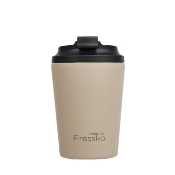 A reusable coffee cup in a light oat brown with a black lid and the text 'made by Fressko' on the bottom.