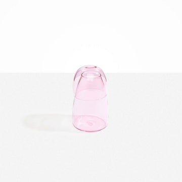 A glass carafe in pink with the cup over the bottle.
