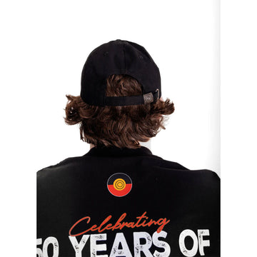 Close up front view of a man wearing a black cap with the text 'The Next Generation Strength Vision Legacy'.