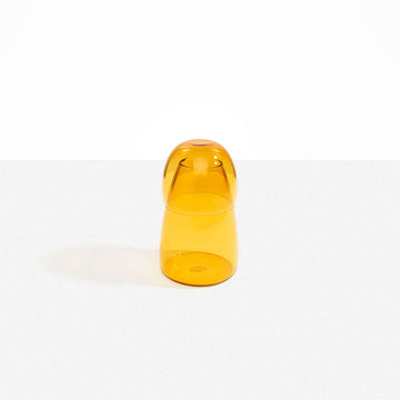 A glass carafe in yellow with the cup over the bottle.