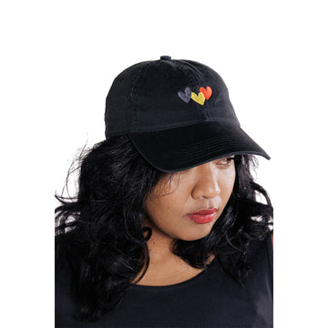 Close up front view of a woman wearing a black cap with black, yellow and red hearts.