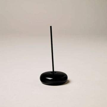 A black glass incense holder with an incense stick.