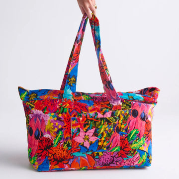 A velvet bag printed with colourful floral motifs is being held up by the handles.