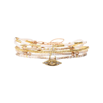 A stack of beaded bracelets in gold and beige colours with a gold eye pendant.