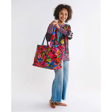 A velvet bag printed with colourful floral motifs is being held up by the handles.