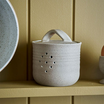 A ceramic container with a lid and holes on the front.