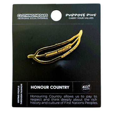 A gold pin shaped like an outline of a gum leaf with the text 'Honour Country' int he middle attached to a black card.