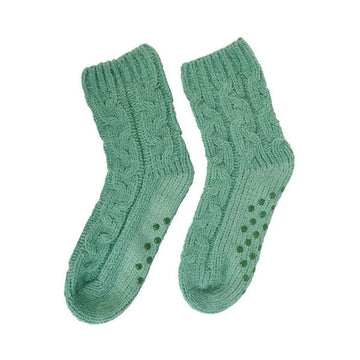 A pair of knitted cable socks in sage green with round grip pieces on the soles.