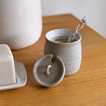 A sugar bowl with a spoon inside and matching lid on a wooden surface.