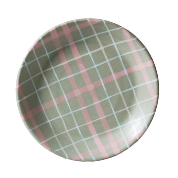 Round ceramic plate with pink and green plaid pattern on a white background.