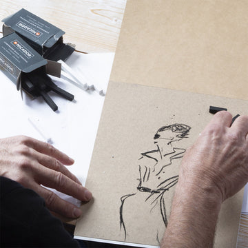 A small black box with the heading 'Compressed White Charcoal' and three white charcoal sticks in front of the box.