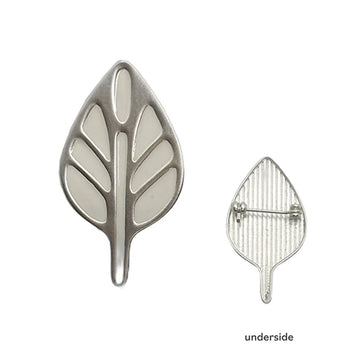A silver brooch in the shape of a leaf and a second brooch showing the pin on the underside.