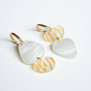 A pair of gold hoop earrings with two irregular shaped round shapes linked together in shades of white and orange.