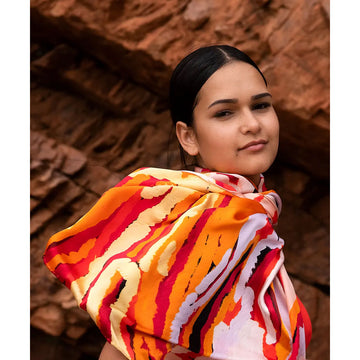 A silk scarf laying flat and printed with artowrk in shades of orange by Katarra Butler Napaltjarri.