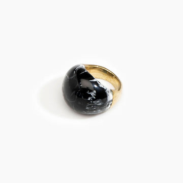 A brass ring with a large resin design on the front in black marble.