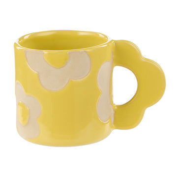 A ceramic mug in yellow with a flower shaped handle and light yellow flowers on the mug.