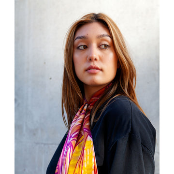 A silk twilly scarf printed with artwork by Sonia Kurarra in red, orange and purple.