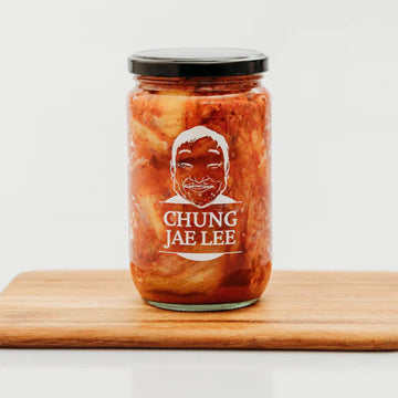 Jar of Kimchi by Chung Jae Lee on a wooden board with a white background.