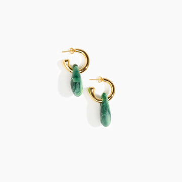 A pair of brass hoop earrings with large moss green resin beads hanging off the hoop.