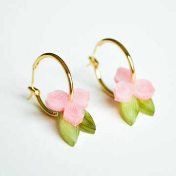 A pair of gold hoop earrings layered with a pink flowers and green leaves through the hoop.