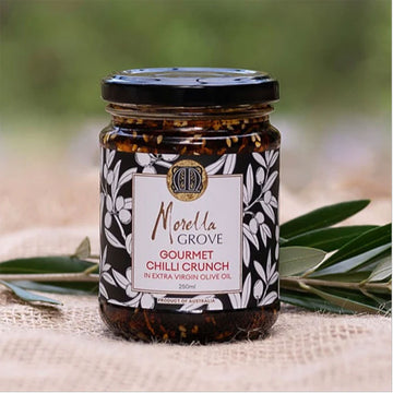 A jar of chilli crunch in olive oil with a product label and olive leaves.