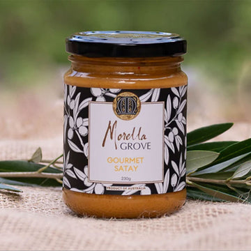 A jar of satay sauce with a product label and olive leaves.