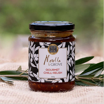 A jar of chilli relish with a product label and olive leaves.