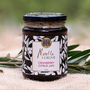 A jar of cranberry citrus jam with a product label and olive leaves.