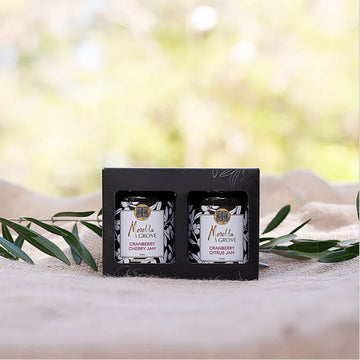 A boxed set of two jars of jam displayed on a linen cloth with olive leaves.