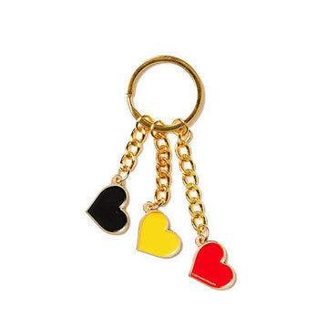 A gold keyring with three different heart charms attached, one in black, one in yellow and one in red.