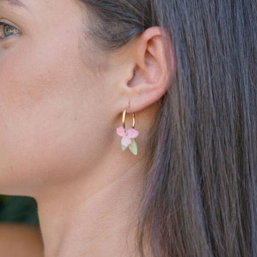 A pair of gold hoop earrings layered with a pink flowers and green leaves through the hoop.