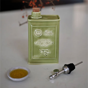 A sage green ceramic bottle designed to hold olive oil with a bottle pourer and small bowl of olive oil.