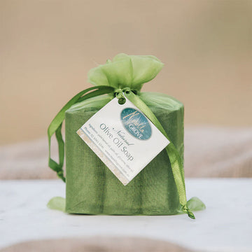 A green organza bag with three bars of soap inside and a label which says 'Natural Olive Oil Soap'.