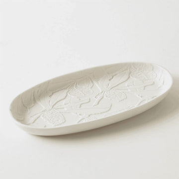 White ceramic platter with embossed leaf patterns on a light gray background.