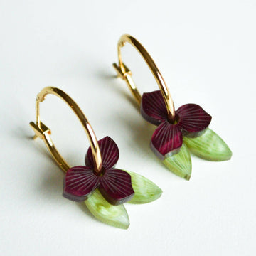 A pair of gold hoop earrings layered with a burgundy flowers and green leaves through the hoop.