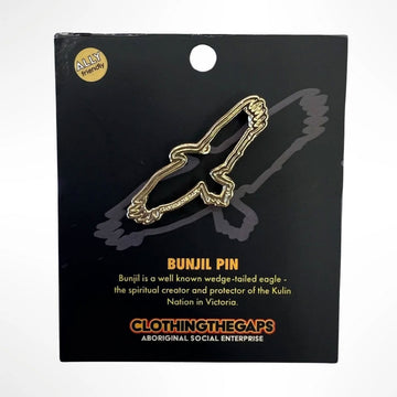 A gold pin in the shape of a eagle attached to a black card with information about the Bunjil eagle.