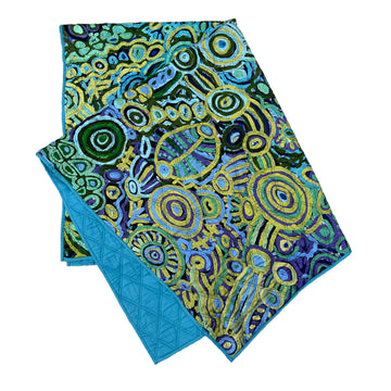 A quilted blanket printed with artwork by Cedric Varcoe in blue and yellow on the front and plain blue on the back.
