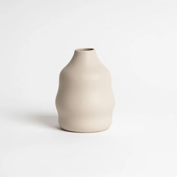 A small ceramic vase in a cashmere colour with two bumps around the sides.