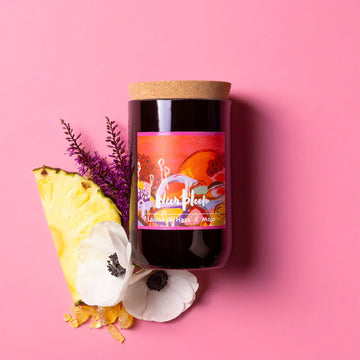 Candle with floral and pineapple elements on a pink background.