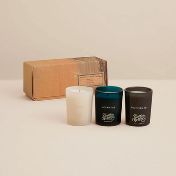 Three candles with labels and a cardboard box on a beige background.