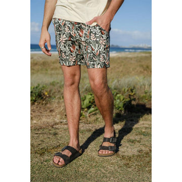 Front close up view of a man wearing protea floral printed shorts in red and green.